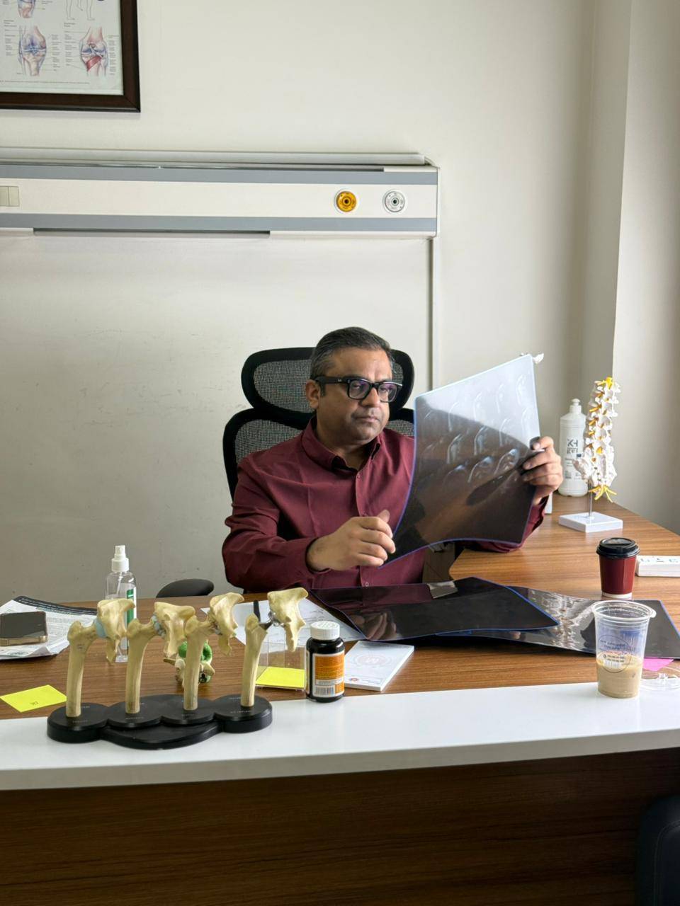 Dr. Ankur Singh reviewing diagnostic MRI and joint scans at clinic desk